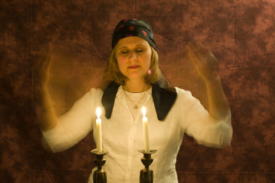 A Traditional Orthodox Jewish Woman With Hair Covered By A Scarf Holds A Match And Light The Sabbath Candles.