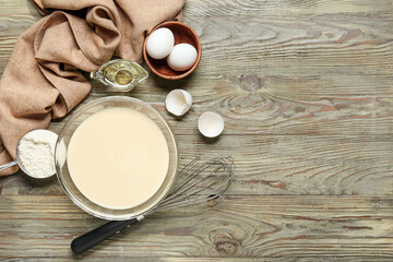 Raw batter with whisk and ingredients on wooden background