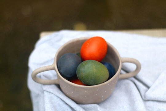 Ceramic bowl filled with painted Easter egss in jewel tones. Selective focus.