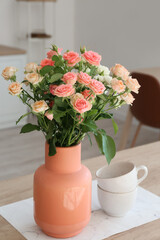 Beige vase with beautiful roses and cups on counter in kitchen