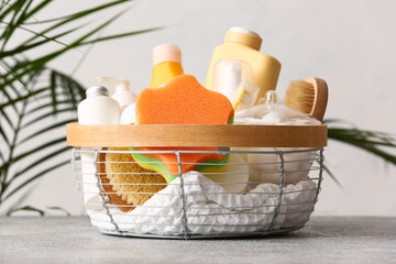 Basket with different bath accessories and cosmetics on table near light wall
