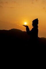 Silhouette of a girl holding the sun with a mountain backdrop.Her eyes looked at the sun as if she saw success.Side facing woman silhouette.
