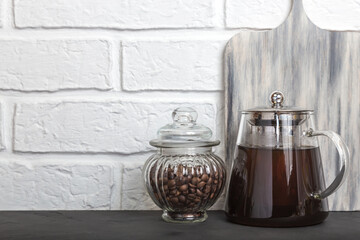 Glass coffee pot with hot coffee drink and coffee beans in a jar on a kitchen countertop. Food background with kitchen utensils with copy space. Front view