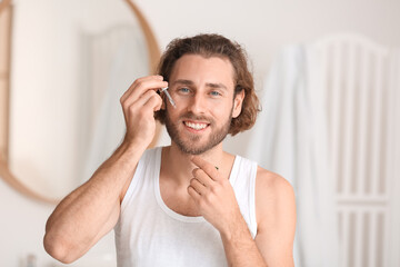 Young man using serum for skin care in bathroom