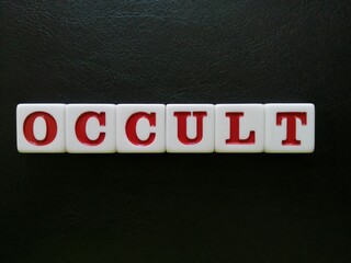 The word Occult is spelled with white and red tiles on a black leather background sheet