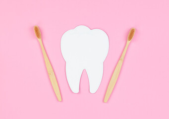 White tooth and wooden toothbrushes on a pink background. Dental care concept, banner, copy space