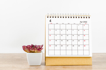 April 2022 desk calendar with plant pot on wooden table.