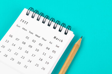 March 2022 desk calendar with wooden pencil on light blue background.