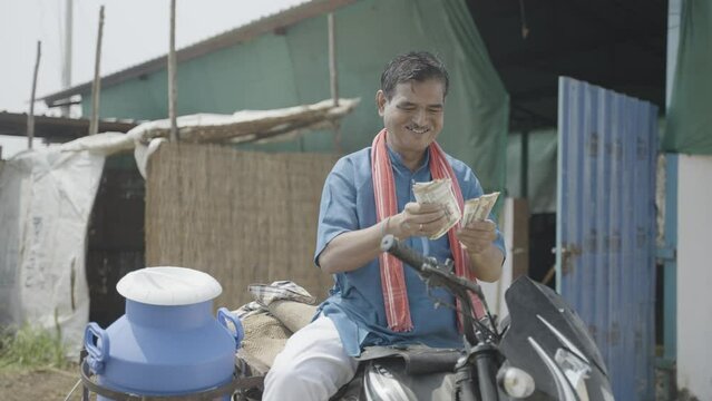 Happy milk dairy farmer couting earnings from dairy production while on bike at farm - concept of profitable business and financial or banking support
