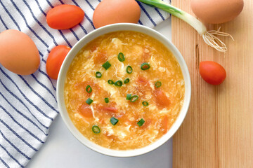 Tomato egg drop soup in a white bowl. Traditional Chinese food. Flat lay top view photo. Food from above concept.	
