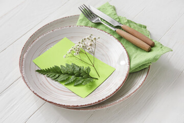 Stylish simple table setting with flowers on light wooden background