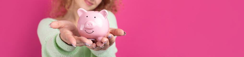 A cute young girl with curly red hair holds a piggy bank, a pink piglet in her hands. The concept of wealth and safety of money.