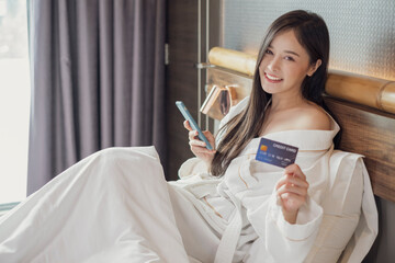 Beautiful woman using smartphone in the morning shopping online. Female playing with smartphone while lying on bed. Asian girl relaxing on bed and playing with the mobile phone.