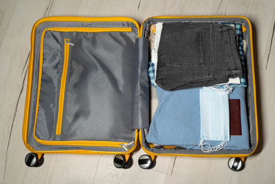 Packing suitcase. Yellow plastic travel bag. Clothes for a trip  journey vacation. Tourism concept. Clothing  passport and face fask. Clothing bag on wheels.