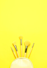Composition with set of makeup brushes in bag on yellow background
