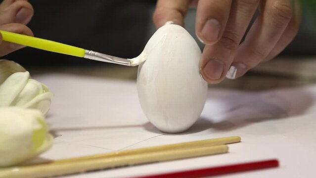 Close-up. Hands paint the Easter egg with a brush pink on a white background. Holiday concept