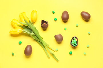Delicious chocolate eggs, beautiful tulip flowers and candies on yellow background
