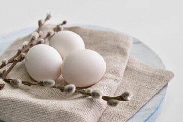Wooden board with fresh chicken eggs and pussy willow branches on light background, closeup