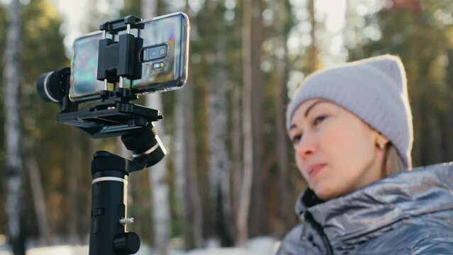The Woman Professional Videographer Holding Smartphone on 3-axis Gimbal Stabilization Device in Winter. Pro Equipment Helps to Make High Quality Video on Phone. Cinematographer Operator. Slow Motion