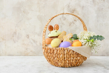 Fototapeta na wymiar Gift basket with painted Easter eggs and flowers on light background