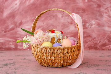 Fototapeta na wymiar Gift basket with painted Easter eggs, flowers and cake on pink background