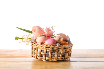 Gift basket with painted Easter eggs and flowers on table against white background