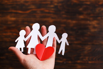 human hand holding happy paper cut family with red heart on a brown wooden background