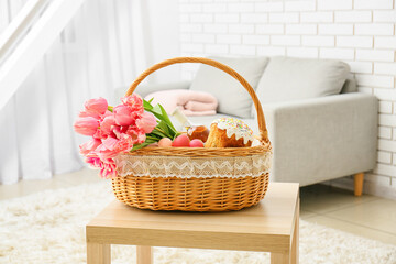 Fototapeta na wymiar Gift basket with painted Easter eggs, tulip flowers, wine bottle and cake on table in room