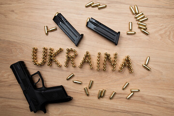 Napis ukraina ułożony z naboi na stole, wokół rozrzucone naboje, broń krótka oraz dwa załadowane magazynki
