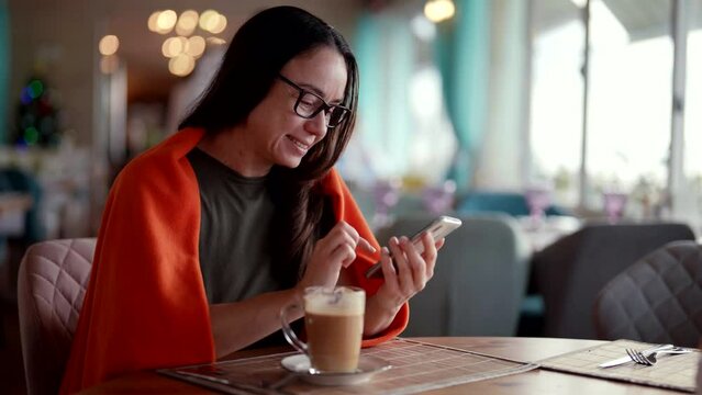 female visitor in restaurant in lunch time, drinking latte and chatting by smartphone