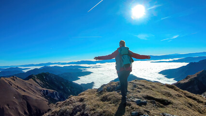 A woman spreading her arms over a panoramic view from mount Eisenerzer Reichenstein in Styria,Austria, Europe.The Ennstal valley is covered in clouds.Hiking trail,Wanderlust. Sunny day.Freedom concept