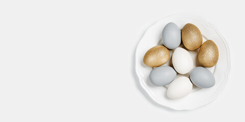Dyed Easter eggs pastel colors shiny golden, gray on round white plate. Happy Easter holiday, celebration food concept, chicken egg white beige shades, trendy color. Top view banner