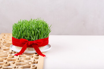 Green fresh semeni sabzi wheat grass in white plate decorated with red ribbon with wooden shebeke...