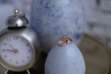 Wedding rings on a nightstand with a clock and a vase.
