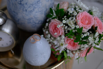 Wedding rings on a nightstand with a clock and a vase.
