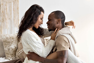 A couple in love - a black man and a woman on a bed in a bright room. Diverse family