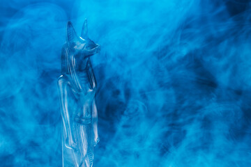 Egyptian statue of the god of death Anubis made of black stone in a blue fog on a black background