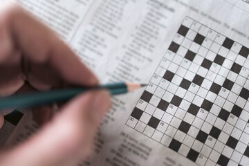Close up hand holding pencil over crossword puzzle on newspaper. Game on for writing some letters...