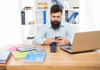 Serious businessman texting sms on mobile phone sitting at office desk