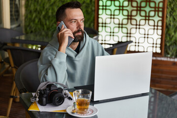 Thoughtful young adult man in casual clothes in cafe talking on a mobile phone