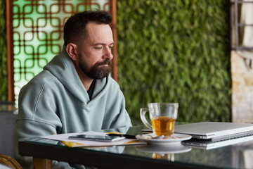 Upset young adult man in casual clothes in cafe with laptop. Online business