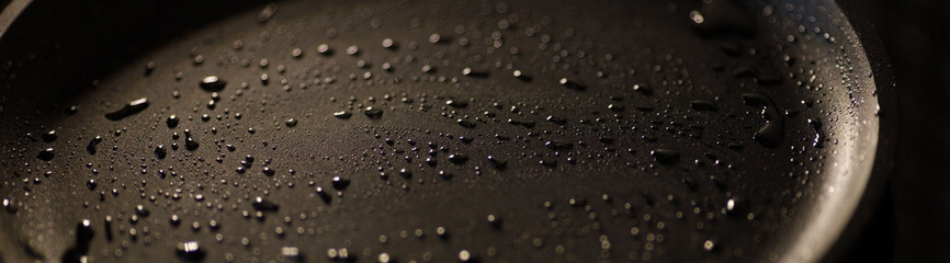 Part of empty cast iron pan of black color with drops of vegetable oil. Close-up. Dark background. Start cooking. banner