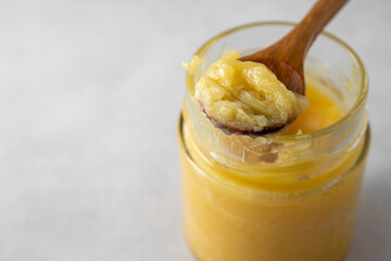 Ghee in a glass jar made with sunflower oil on a light background, copy space for text. Hard light.