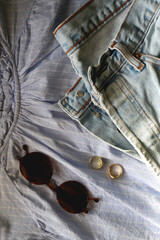 Blue striped blouse, light wash jeans, round sunglasses and gold rings. Flat lay.