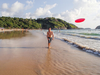 Man is playing with frisbee on Nai Harn beach on Phuket island. Leisure activity outdoors. Thailand. - Powered by Adobe