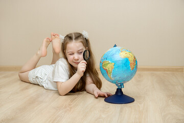 little girl lies on the floor and squints at the globe through a magnifying glass