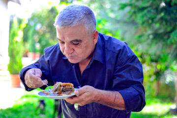 Man eating turkish baklava on a plate on sunny summer day in a backyard