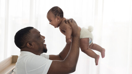 Dark skinned father holding cute little baby girl up in the air. Playing and bonding time with daughter. Happiness and love, Father's day concept.
