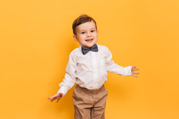 A studio shot of a cute little boy grimacing stands on a yellow background. Funny kid