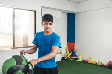 A young man does weighted oblique twists with a wall ball with handles. Core or cardio workout at...